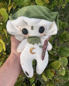 a hand holding a white stuffed animal with a green hat on it's head