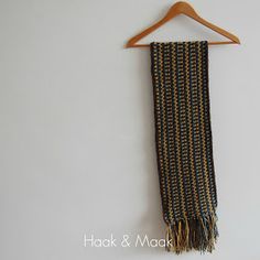 a black and gold scarf hanging on a wooden hanger next to a white wall