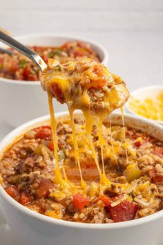 a spoon full of chili cheese soup being lifted from a white bowl with other bowls in the background