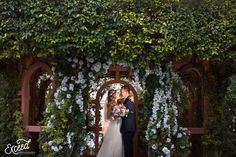 a bride and groom kissing in front of an arch covered with flowers