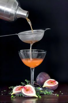 a glass filled with liquid sitting on top of a table next to sliced figs