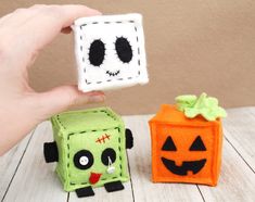 a hand holding a small toy with two faces on it next to an orange and green box