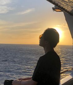 a person sitting on a boat watching the sun go down over the ocean in the distance