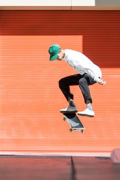 a man flying through the air while riding a skateboard in front of a red wall