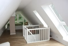 an attic bedroom with white walls and wooden floors, along with a baby crib in the corner