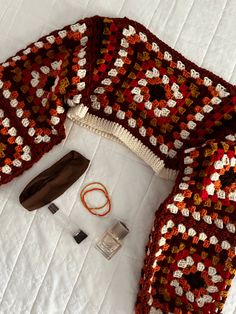 a crocheted sweater and other items are laid out on a white bed sheet