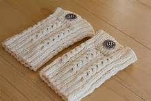 two white knitted mittens sitting on top of a wooden floor