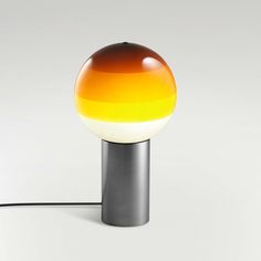 an orange and yellow lamp sitting on top of a white table next to a black cord