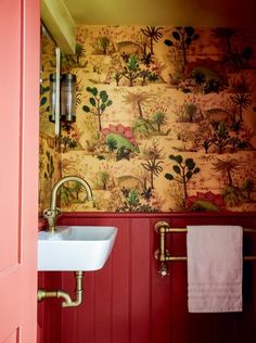 a bathroom with red walls and wallpaper has a sink in the corner next to it