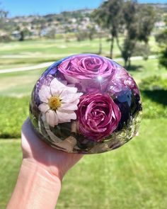 a hand holding up a glass ball with flowers in it on a green lawn area