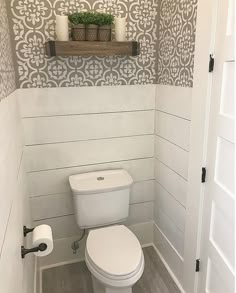 a white toilet sitting inside of a bathroom next to a wooden shelf with candles on it