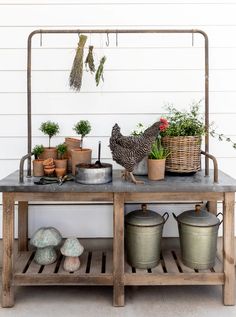 a chicken standing on top of a wooden table next to potted plants and buckets