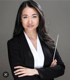 a woman in a black jacket and white shirt is holding a wand with her arms crossed