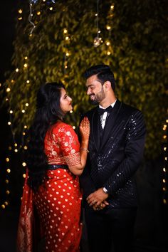 a man and woman standing next to each other in front of trees with lights on them