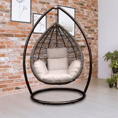 a hanging chair with cushions in front of a brick wall and potted plant on the floor