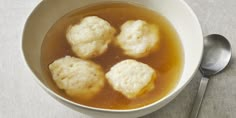 three dumplings are in a bowl of soup with a spoon on the table next to it