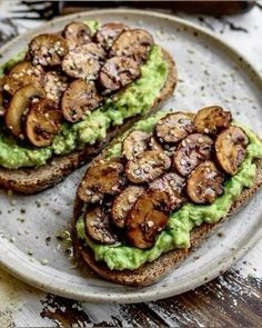 two slices of toast with avocado and mushrooms on it sitting on a plate