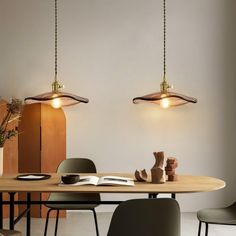 two pendant lights hanging over a table in a room with chairs and a book on it