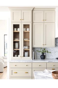 a kitchen with white cabinets and marble counter tops, gold pulls on the cupboards