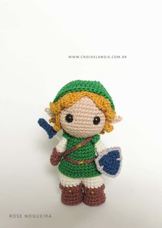 a crocheted doll with a green hat holding a blue arrow and a shield