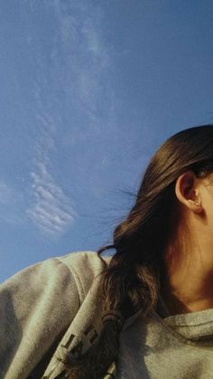 a woman is flying a kite in the sky with her hair pulled back and looking up