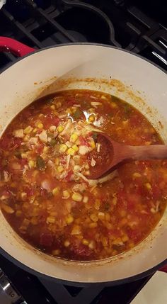 a wooden spoon in a pot filled with corn and tomato soup on top of the stove