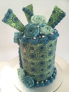 there is a blue and green cake with flowers on the top, sitting on a plate