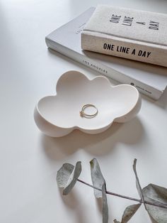 a ring dish sitting on top of a table next to a book and some leaves