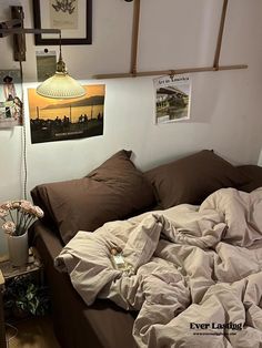 an unmade bed in a small room with pictures on the wall and posters above it