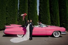 a bride and groom standing in front of a pink car