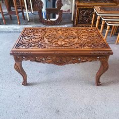 an ornately carved wooden coffee table in front of other antique furniture and mirrors on display