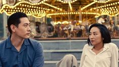 a man and woman sitting on the ground in front of a carousel