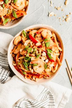 two bowls filled with noodles and vegetables on top of a white towel next to chopsticks