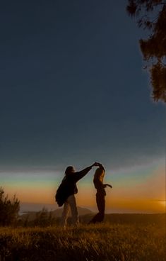 two people standing on top of a grass covered hillside under a blue sky at sunset