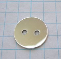 a metal button sitting on top of a piece of paper with two holes in it