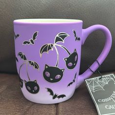 a purple coffee mug with black cats and bats on it, next to a card