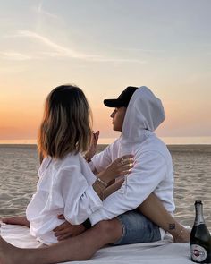 two people sitting on the beach, one with a bottle of beer