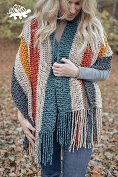 a woman standing in leaves wearing a multicolored crocheted shawl with fringes