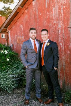 two men standing next to each other in front of a barn