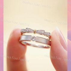 a woman's hand holding a wedding ring with two diamonds on top of it