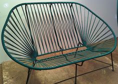 a green metal bench sitting on top of a cement floor