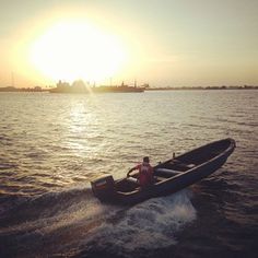 a man riding on the back of a boat in the middle of water at sunset