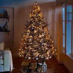 a lit christmas tree in a living room with presents on the floor next to it