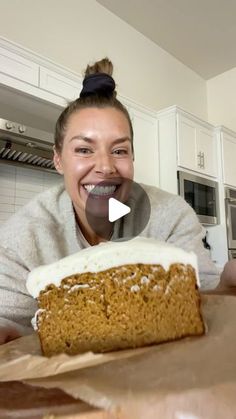 a woman smiling and holding a piece of cake in front of her face while sitting at a kitchen counter