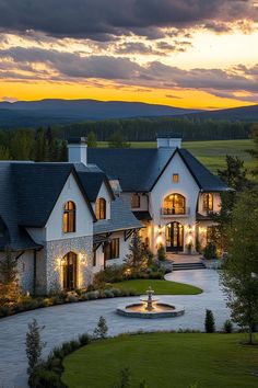 a large white house with a fountain in the front yard at sunset or dawn, surrounded by lush green grass and trees