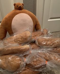 a teddy bear sitting on top of a pile of baguets in plastic bags