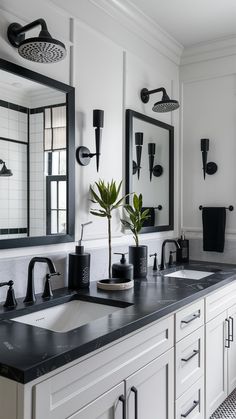 a black and white bathroom with double sinks, mirrors and plants on the countertop