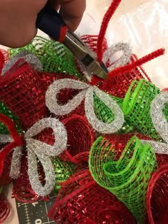 someone is cutting ribbon with scissors on top of some red and green christmas mesh balls