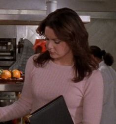 a woman in a pink sweater is holding a black folder and looking at an orange