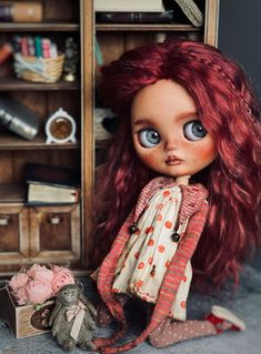 a doll with red hair sitting on the floor next to a bookcase and stuffed animal